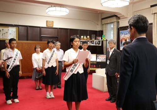 内閣総理大臣メッセージを読み上げる長友さんと拝聴する知事の写真