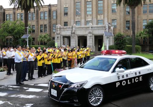 交通安全運動へ出発するパトカーと見送る人々の写真